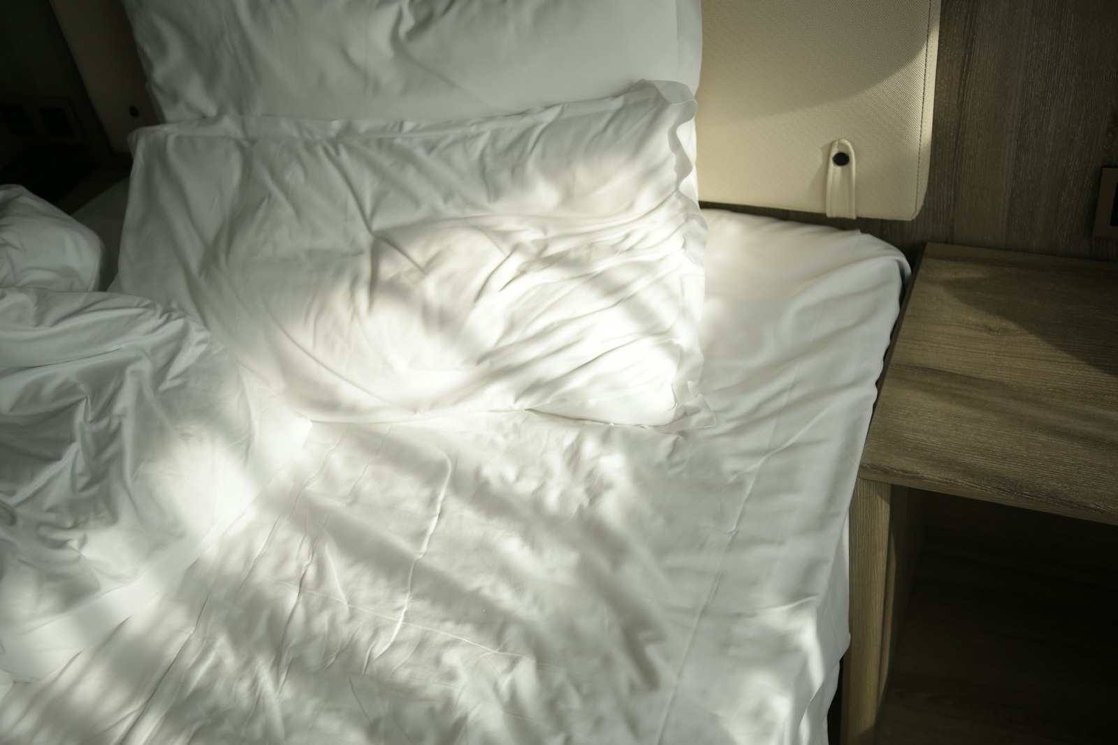 A rumpled white bed in a quiet, sunlit bedroom